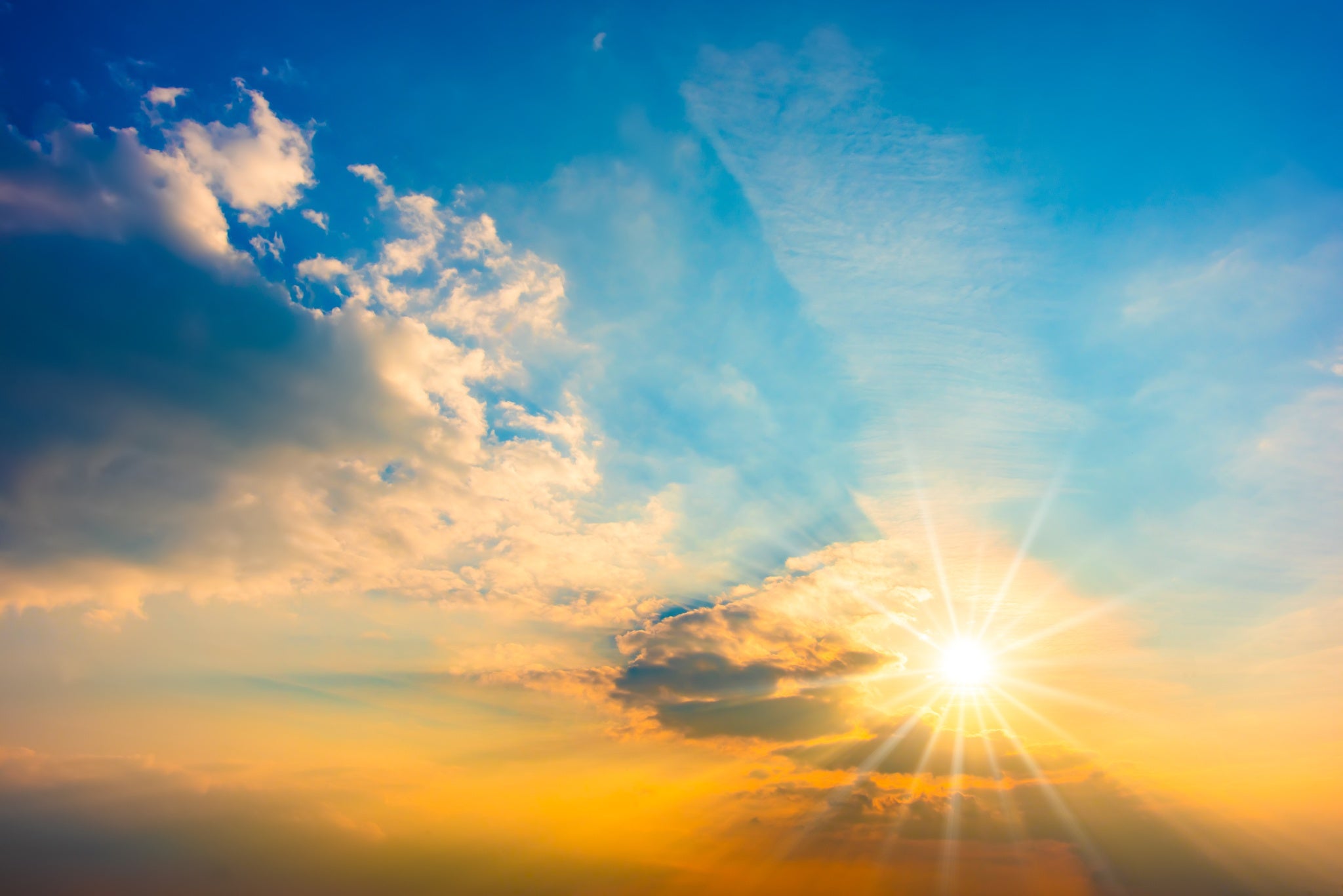 photo of the sun coming through the clouds of a blue sky